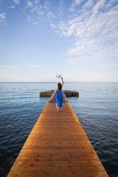 Montenegro, Budva. A girl in a blue dress lies on a wooden pier near the sea, a beautiful sky with clouds. Vacation concept, travel to Europe