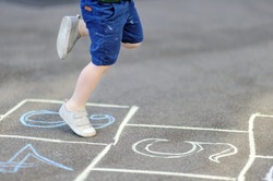 Closeup of little boy's legs and hopscotch drawn on asphalt. Child playing hopscotch game on playground outdoors on a sunny day. Summer activities for children.
