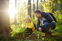 School boy and his father hiking together and exploring nature with magnifying glass. Child with his dad spend quality family time together in the sunny summer forest. Daddy and his little son