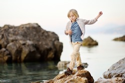 Cute schoolchild hiking by rocks near sea, having fun and exploring nature. Concepts of adventure, scouting and hiking tourism for kids.