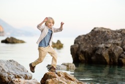 Cute schoolchild hiking by rocks near sea, having fun and exploring nature. Concepts of adventure, scouting and hiking tourism for kids.