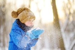 Little boy blowing snow from his hands. Child enjoy walking in the park on snowy day. Baby having fun during snowfall. Outdoor winter activities for family with kids.