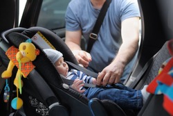 Father fasten his little son in car seat