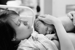 Black and white shot of young woman with newborn baby right after delivery