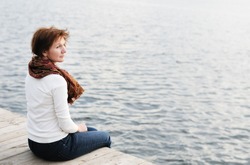 Middle age woman sitting on wood boards by the water