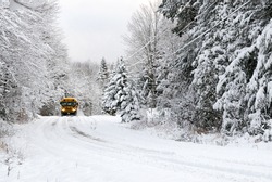 A school bus drives down a snow covered rural country road lined with snow covered trees after a snow storm during the winter season. 