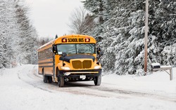 A school bus drives down a snow covered rural country road lined with snow covered trees after a snow storm during the winter season.  Series 3 of 3 