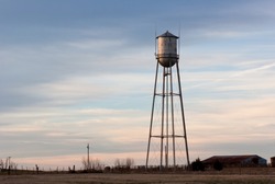 Old small town water tower, lit by sunlight from the left side and set against a cloudy sky at dusk.