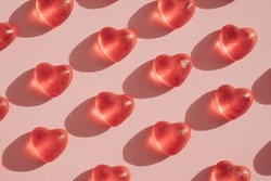 Red transparent gummy candy hearts pattern on light pink background. Valentines day minimal concept