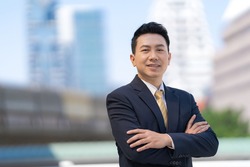 Portrait of successful asian businessman standing with arms crossed standing in front of modern office buildings
