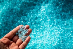 A hand hold or touching plastic pellets , plastic polymer dye granules color clear blue