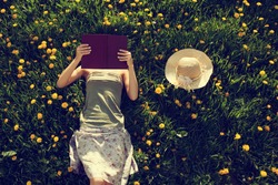Girl lying in grass, reading a book. Intentionally toned.