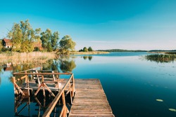 Old Wooden Fishing Pier Near Summer Lake Or River. Calm Water In Beautiful Summer Sunny Day