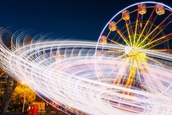 Rotating In Natural Motion Effect Illuminated Attraction Ferris Wheel On Summer Evening In City Amusement Park.