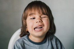 Portrait of adorable 3 year old kid learning to wink his eye. Cute caucasian boy with funny face expression. Real child having fun indoors with family. Healthy and happy childhood. Parenting concept.