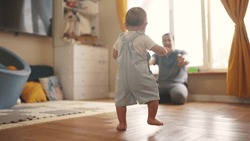 baby first steps. baby goes her father at window learns to walk to take first steps. happy family kid dream concept. dad calls son baby first steps indoors. happy family lifestyle indoors concept