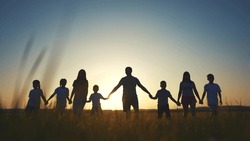 large family walks across field holding hands. happy family childhood dream concept. family walks across the field on the grass lifestyle at sunset and hold each other's hands dark silhouettes