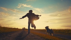 teen girl running with dog in the park. happy family freedom a kid dream concept. silhouette of a teenage girl running along the road in the park at sunset view from the back sun with a shaggy dog