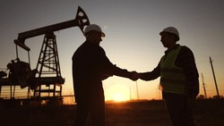 handshake business oil contract. handshake worker and businessman shaking hands against sunlight the backdrop of an oil pump. oil extraction business concept. silhouette handshake contract