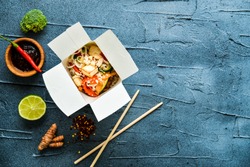 thai noodle in paper box with fried vegetables on gray concrete background. top view flat lay with copy space. street food to go