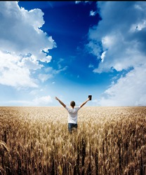 man holding up Bible in a wheat field
