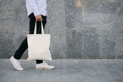 Young man holding white textile eco bag against urban city background. . Ecology or environment protection concept. White eco bag for mock up.