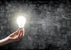 hand holding or showing a light bulb in front of  business idea concept on wall backboard blackground