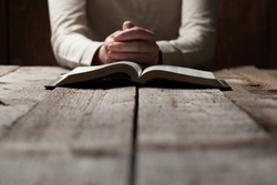 Woman hands praying with a bible in a dark over wooden table