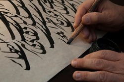 A calligrapher writing with pen and ink. man hands writing arabic calligraphy with ink. Arabic and Persian calligraphy. Abstract and unclear writing. A writing of repeating the letters 