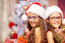 Happy sisters holding gifts in front of christmas tree
