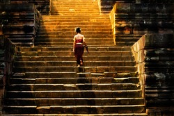 Girl climbing up stairs of castle stone. She walking slow step, go to the big door. The sun is shining to the stairs in the morning. All wall is make by stone. It is ancient building style.