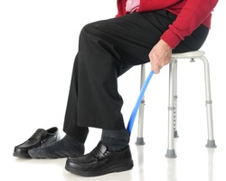 Close-up view of a senior man sliding into his loafers with the aid of a long-handled shoe horn.  On a white background.