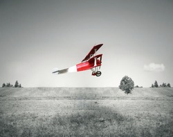 Fantasy flight of an old red airplane flying on a field and sky in black and white