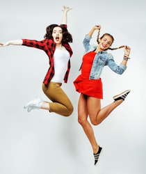 two pretty brunette and blonde teenage girl friends jumping happy smiling on white background, lifestyle people concept
