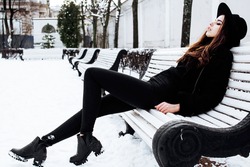 young pretty modern hipster girl waiting on bench at winter snow park alone, lifestyle people concept
