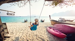 Happy woman on the swing at the tropical beach on Phi Phi Island in Southern Thailand. Travel magazine concept.