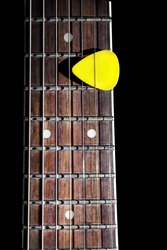 Yellow guitar pick on the fingerboard close up isolated on black background