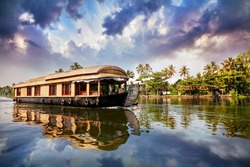 House boat in backwaters near palms at cloudy blue sky in Alappuzha, Kerala, India