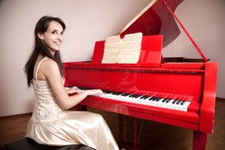 Happy woman in dress playing the red grand piano, smiling and looking at camera