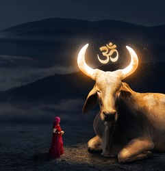 Woman in red sari worships big Holy Cow with glowing horns and Om symbol in Rajasthan, India