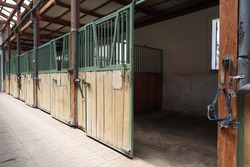 Inside modern clear stable or barn with horse boxes. Passageway view in natural light in the end. Cleared empty stall in the stable keeping sport horses