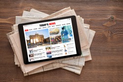 Tablet with news website on stack of newspapers. All contents are made up.