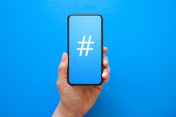 Person holding mobile phone with hashtag symbol on the screen
