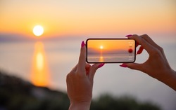 Woman holding mobile phone in hands and taking sunrise photo