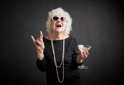 Grandma with glasses and drink in hand showing rock sign 