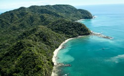 Lush jungle covered mountains stretch out into the Gulf of Nicoya next to the rocky and sandy beach of Ballena Bay in Costa Rica.
