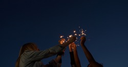 close up of hands of girls holding sparklers . Group of friends celebrating waving sparkler fireworks dancing enjoying party having fun holiday celebration at evening social gathering on rooftop