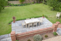 Large UK back garden with lawn and wooden patio furniture on a terrace in summer