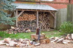 Chopping firewood. Axe and log pile outside a log store in a UK garden