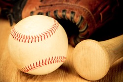 Baseball - This is a close up shot of an old baseball and wooden bad on a wood background with an old glove in the background. Shot in a warm retro color tone.